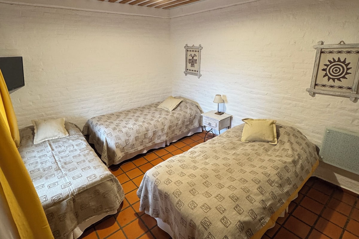 Une chambre avec deux lits simples, une petite table de chevet avec une lampe, une étagère murale décorative et un ventilateur de plafond.