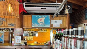 A bar with wooden interiors, a poster of 'Atlantis 84', and a variety of bottles on shelves. - The Paradise (Puerto Piramides)