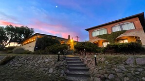 A two-story house with a stone staircase leading to the entrance, surrounded by greenery and a clear sky. - The Paradise (Puerto Piramides)