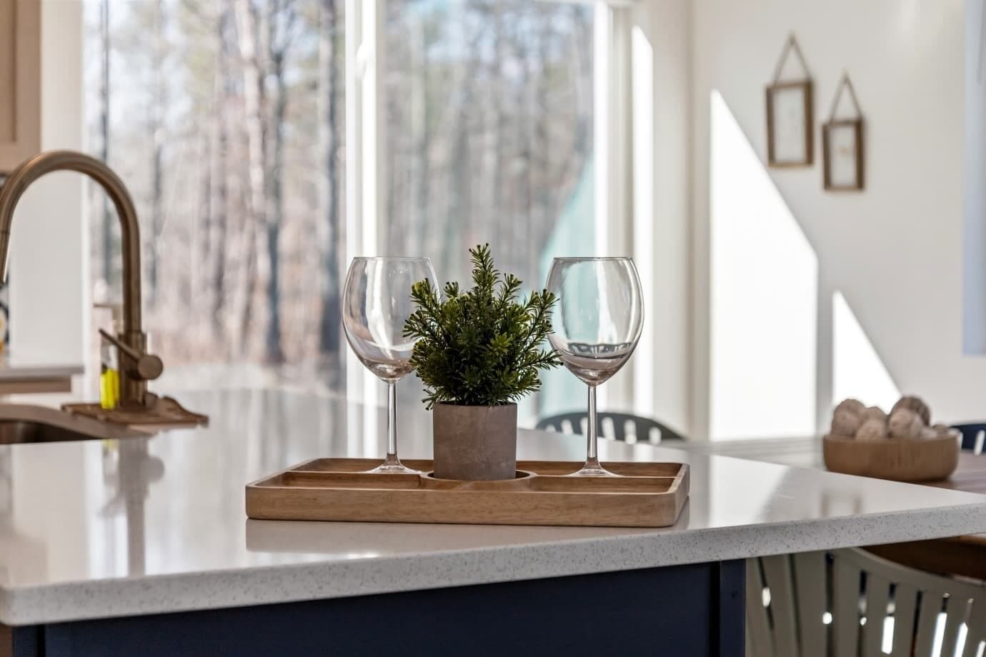 Un comptoir de cuisine avec deux verres à vin, une petite plante en pot et un plateau en bois.