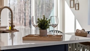 Una encimera de cocina con dos copas de vino, una pequeña planta en maceta y una bandeja de madera.