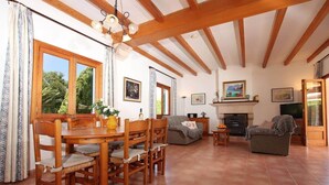 Uma sala de estar ampla com área de jantar, vigas de madeira no teto, lareira e televisão.