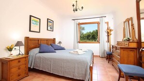 Quarto com cama, duas mesas de cabeceira, cômoda, espelho e janela com vista para o verde.