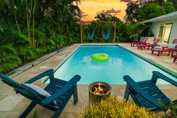 A rectangular pool with a fire pit in the center, surrounded by blue lounge chairs and a hammock.