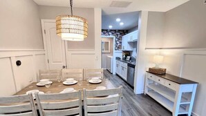 A dining area with a wooden table and chairs, a hanging light fixture, and a white cabinet with drawers. - Chic Chateau-Less than 2 miles to the strip! (Branson)