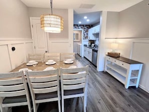 Un coin repas avec une table et des chaises en bois, un luminaire suspendu et un meuble blanc avec des tiroirs.