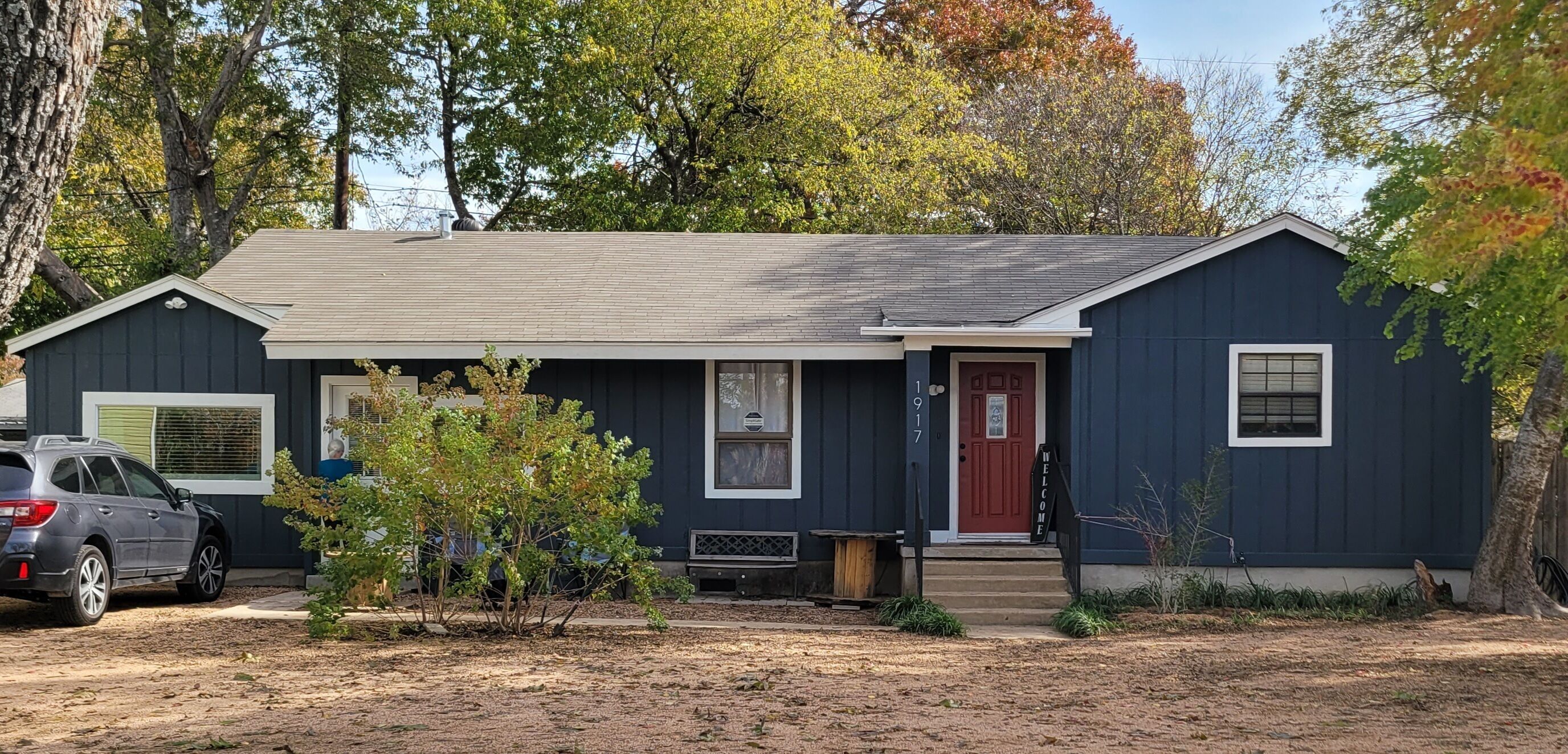 A single-story house with a dark blue exterior, a red front door, and a small porch.