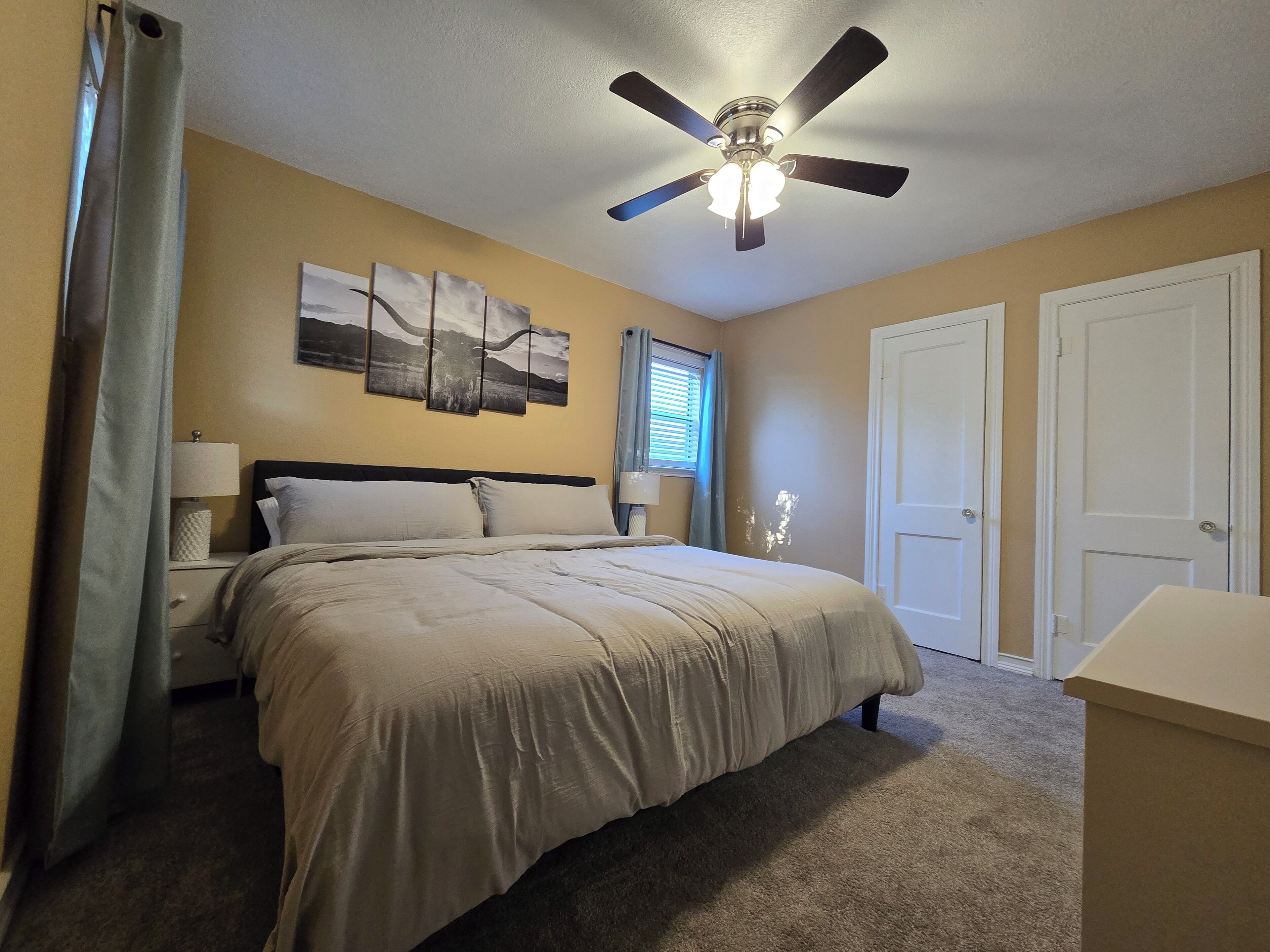 A bedroom with a bed, a ceiling fan, a window with blinds, and a door.