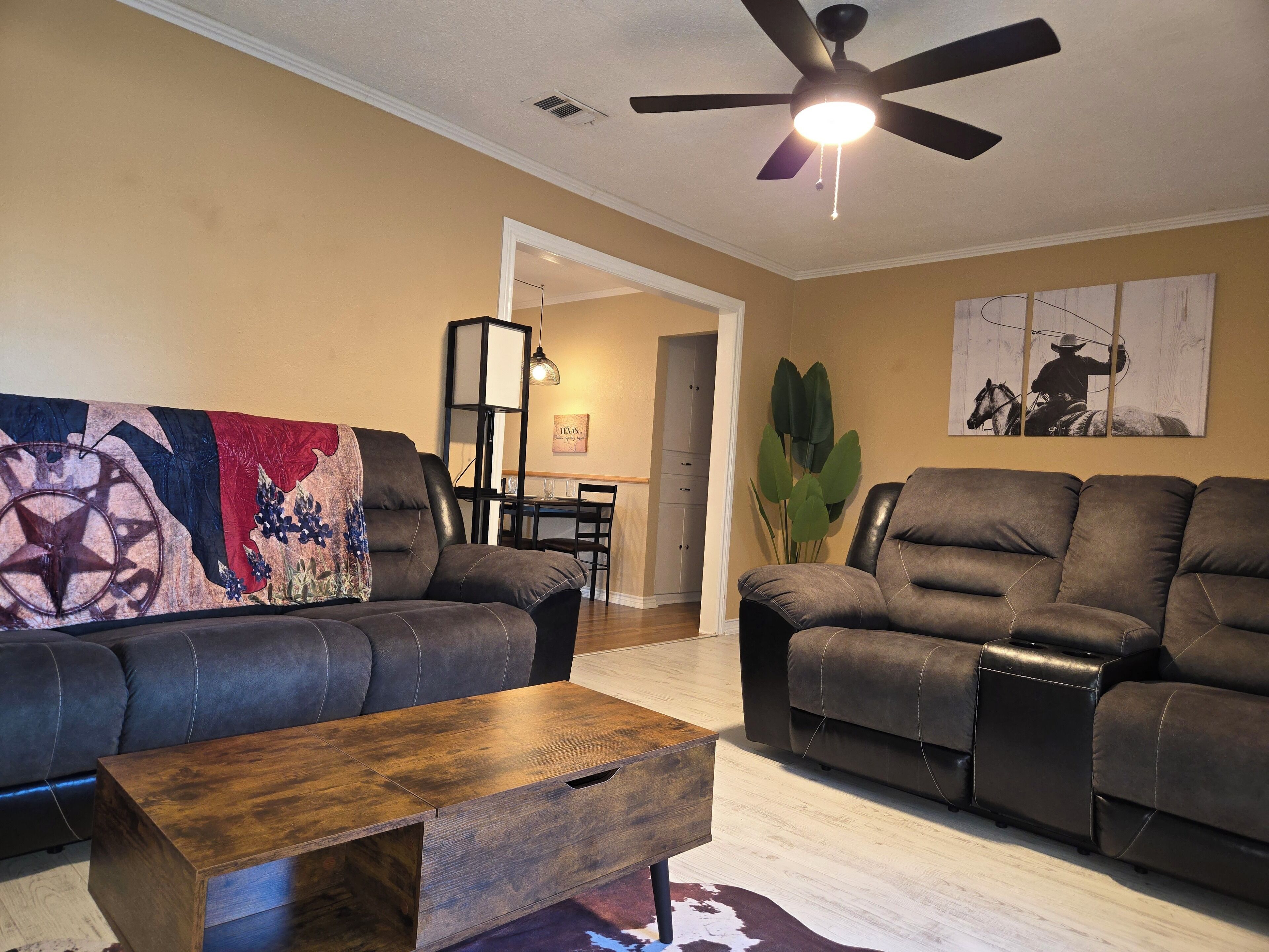 A living room with two sofas, a wooden coffee table, a ceiling fan, and a wall-mounted painting.