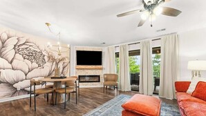 Ein Wohnzimmer mit Kamin, Fernseher, Essbereich mit Stühlen und einer großen Blumenmalerei an der Wand.