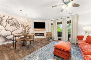 Una sala de estar con chimenea, televisor, comedor con sillas, sofá y un gran mural floral en la pared.