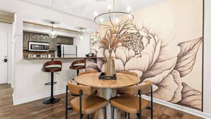 Ein Essbereich mit einem runden Holztisch, sechs Stühlen, einer Chandelierleuchtre und einer großen floralen Wandmalerei.