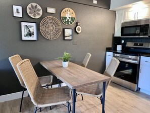 A dining area with a wooden table and wicker chairs, a kitchen with modern appliances, and wall decorations including a 'TAKE A HIKING' sign.