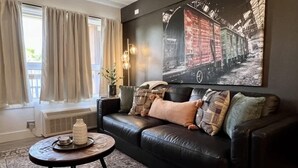 A living room with a black leather sofa, a round coffee table, and a large abstract painting on the wall. - Roark Shores by Branson Landing (Branson)
