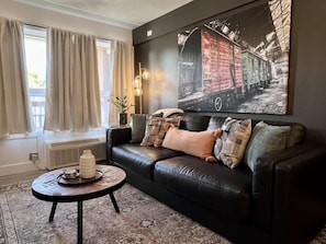 Ein Wohnzimmer mit einer schwarzen Ledersofa, einem runden Couchtisch und einem großen abstrakten Gemälde an der Wand.