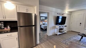 A modern kitchen with stainless steel appliances, a dining area with a wooden table, and a TV in the living room. - Roark Shores by Branson Landing (Branson)