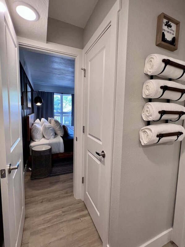 A hotel room with a bed, a bedside lamp, a wall-mounted towel rack, and a door leading to another room.