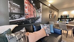 A modern living room with a black leather sofa, a dining area with wicker chairs, and a kitchen in the background. - Roark Shores by Branson Landing (Branson)