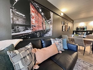 Ein modernes Wohnzimmer mit einer schwarzen Ledersofa, einem Essbereich mit Korbstühlen und einer Küche im Hintergrund.