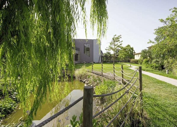 A modern building with a glass facade, surrounded by a grassy area and a small water feature. - Hotiday Maremma Riparbella (Riparbella)