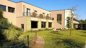 Un edificio moderno con fachada de piedra, una terraza de madera y un césped con sillones de descanso.