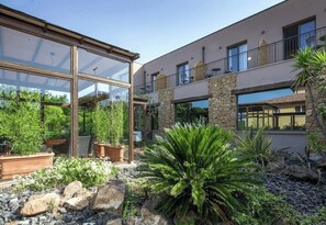 A modern building with a glass conservatory, stone accents, and a landscaped garden with various plants. - Hotiday Maremma Riparbella (Riparbella)