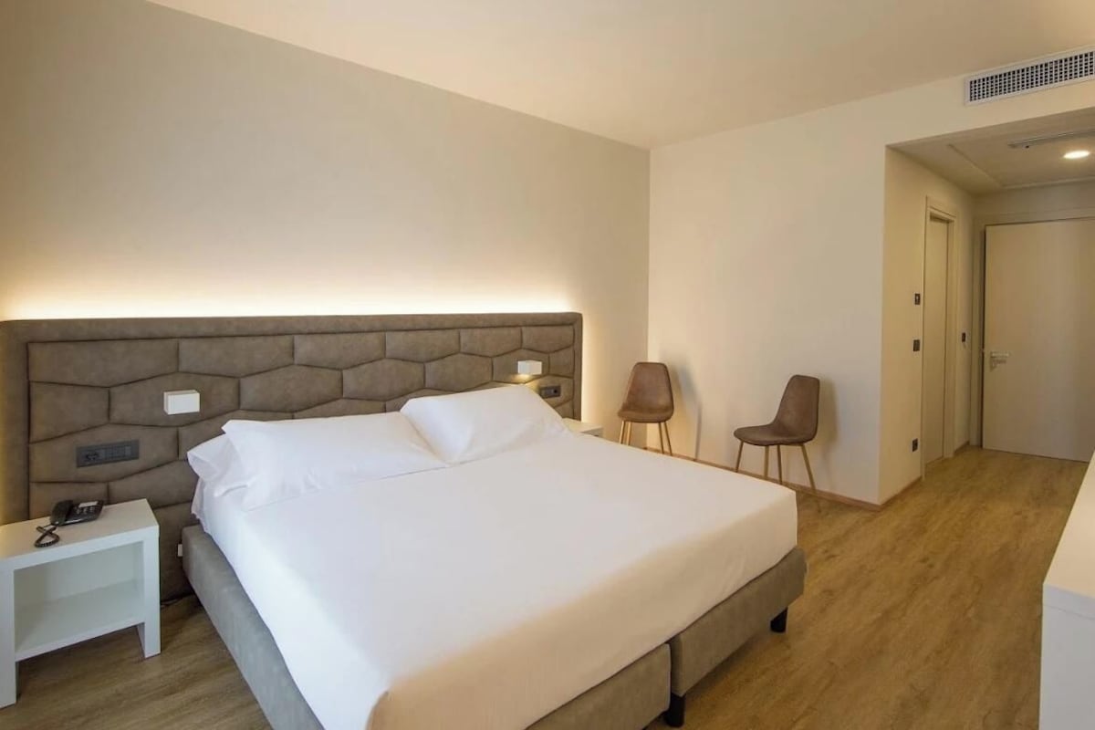 Habitación de hotel con una cama grande, mesitas de noche, un escritorio, dos sillas y una puerta que da a otra habitación.