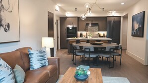 Un salon moderne avec un canapé en cuir marron, une table basse en bois et un coin repas comprenant une table ronde et des chaises.