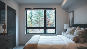 Une chambre avec une grande fenêtre, un lit, une commode et une table de chevet.