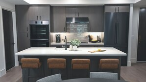Une cuisine moderne avec des meubles de couleur sombre, un îlot central doté de tabourets de bar et une table à manger.