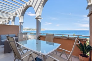 A balcony with a glass table and chairs, overlooking the sea.