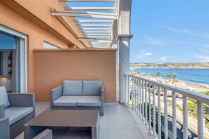 A balcony with a sofa, a table, and a view of the sea.