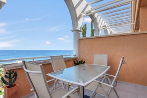 A balcony with a glass table and chairs, a view of the ocean, and a cactus plant.