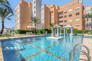 A swimming pool with dividers, palm trees, and a multi-story building in the background.