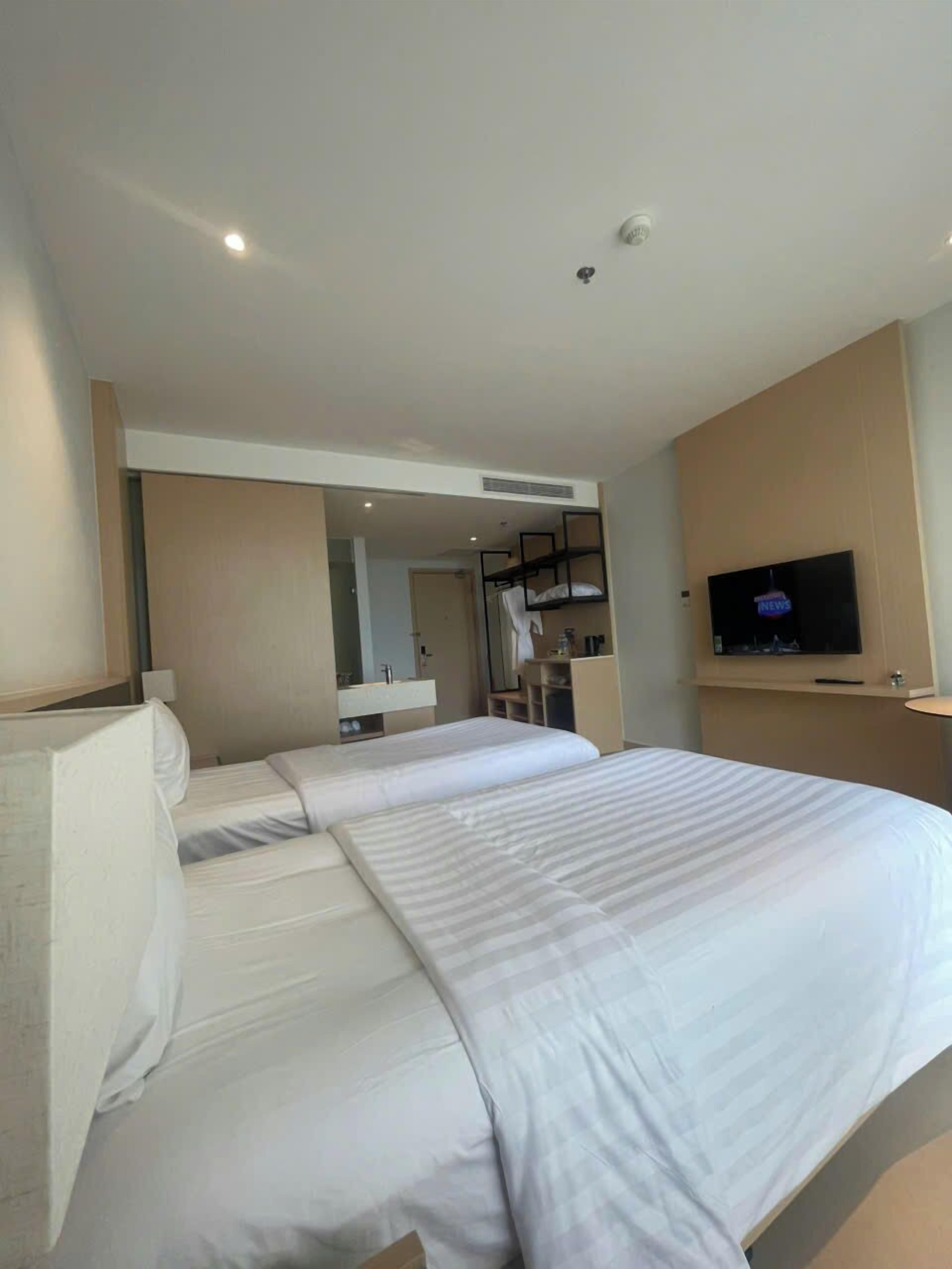 Ein Hotelzimmer mit einem großen Bett, einem an der Wand montierten Fernseher und einem im Hintergrund sichtbaren Badezimmer.