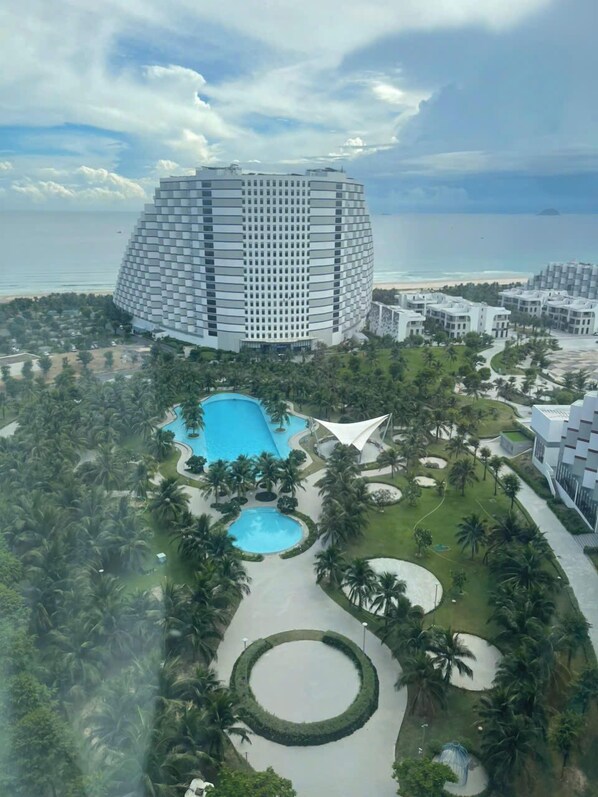 Un hotel moderno con piscina central, rodeado de palmeras y vistas a la playa.