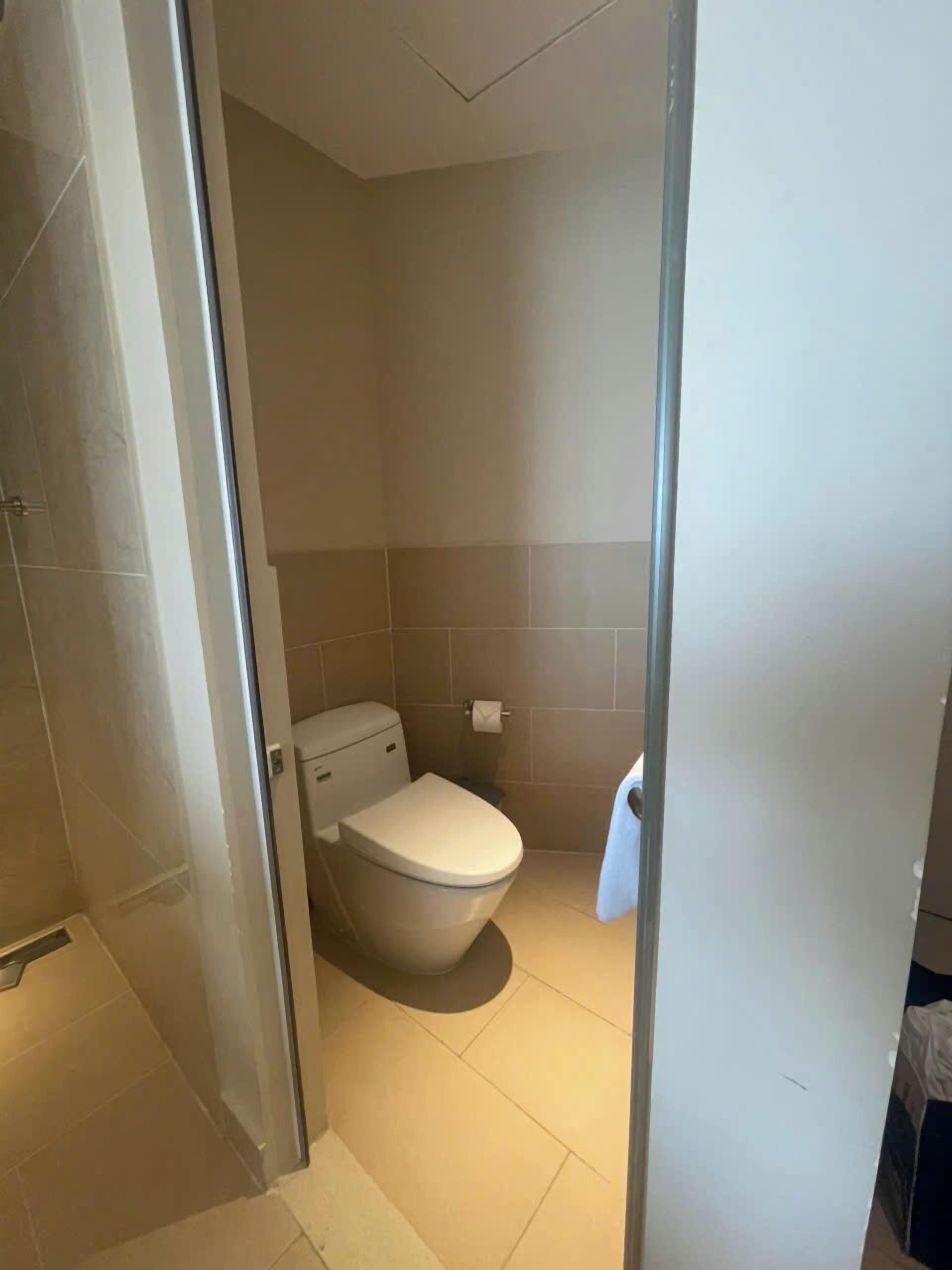 A bathroom with a toilet, a shower area, and a glass door leading to another room.