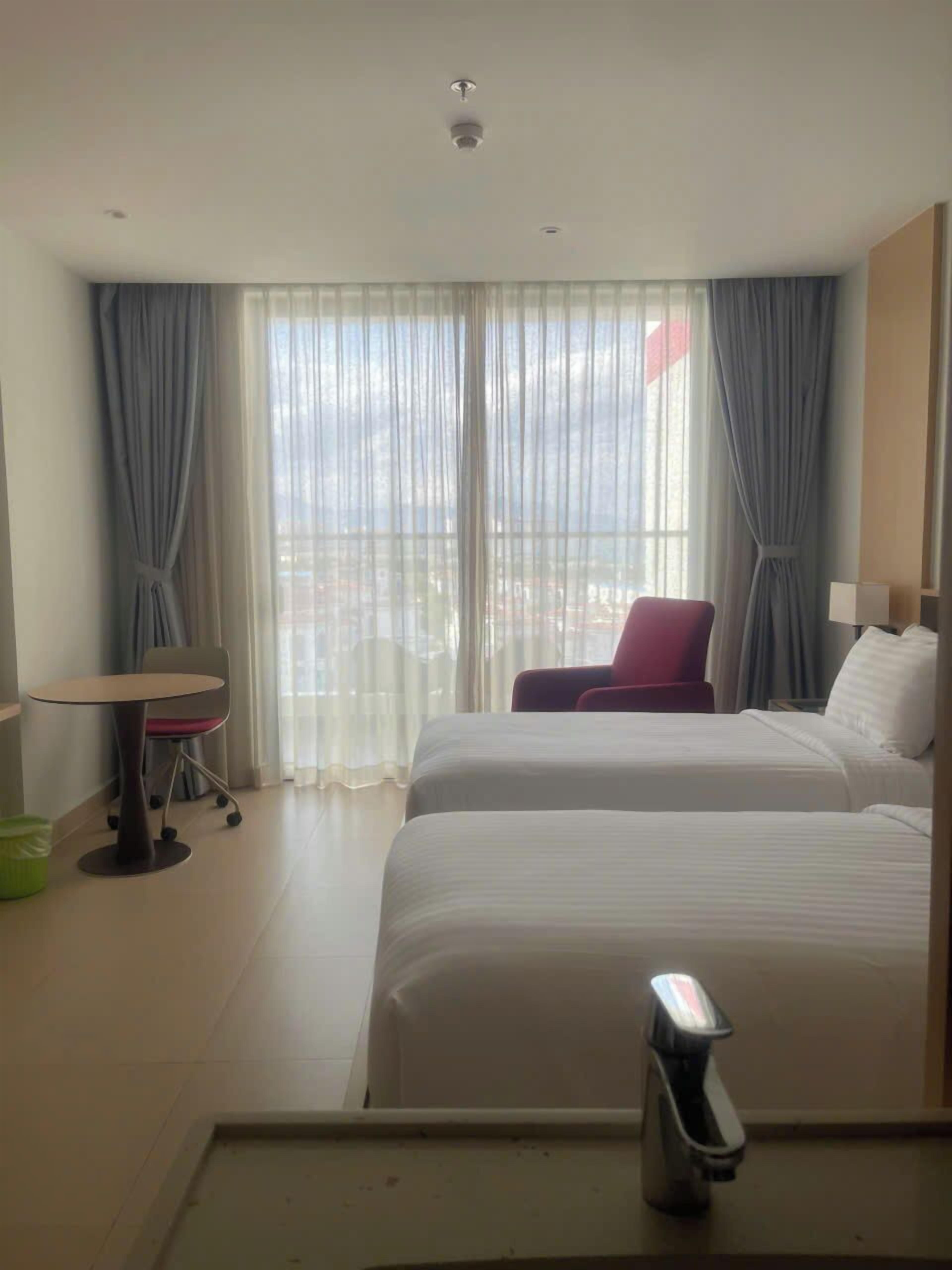 Ein Hotelzimmer mit zwei Betten, einem Schreibtisch, einem Stuhl und einem Vorhangfenster.