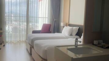 A hotel room with two beds, a large window with curtains, a bathroom with a sink and mirror, and a view of the city.