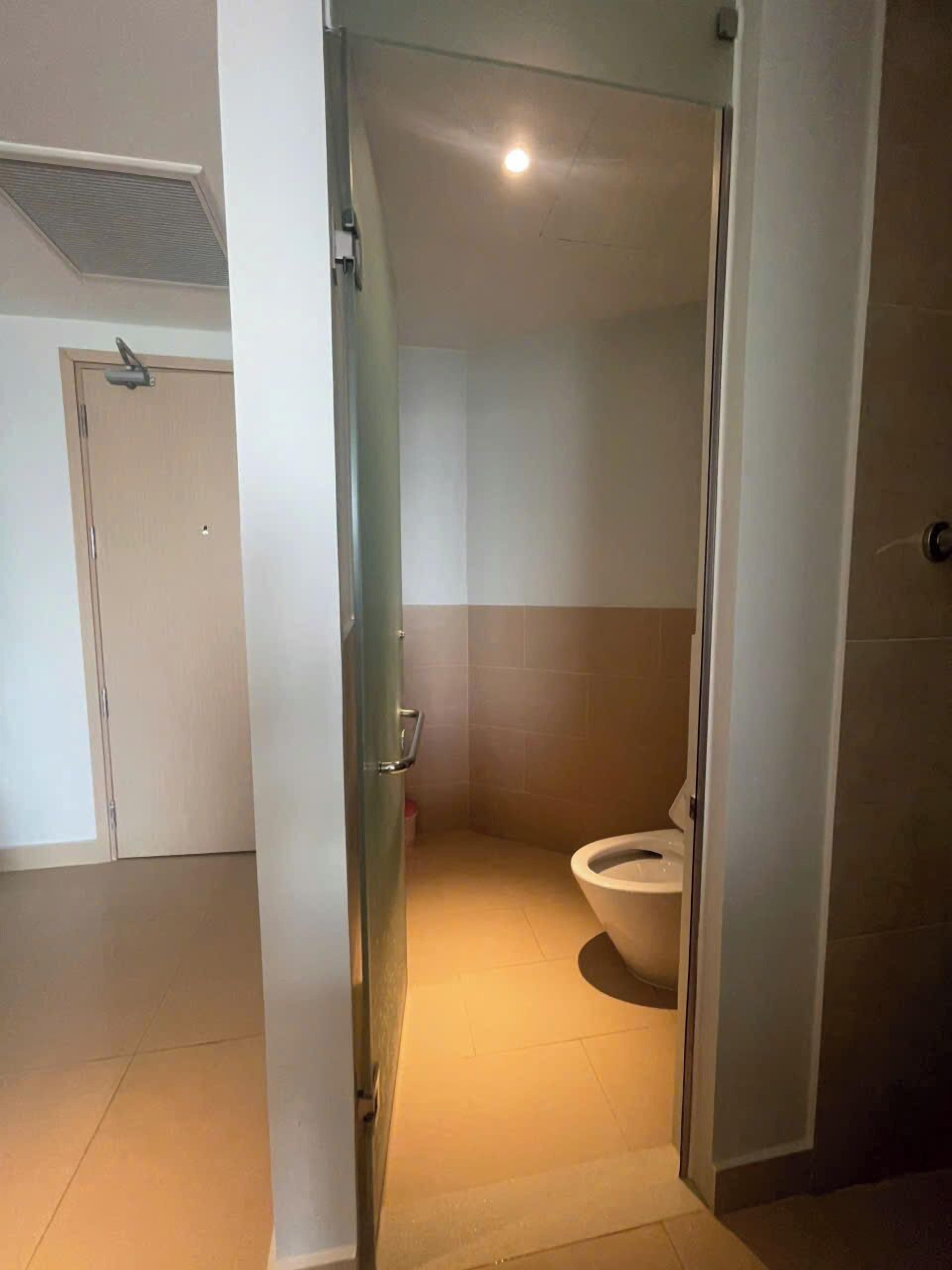 Ein kleines, schmales Badezimmer mit Toilette, einer Glaskabine und einer Tür zu einem weiteren Raum.