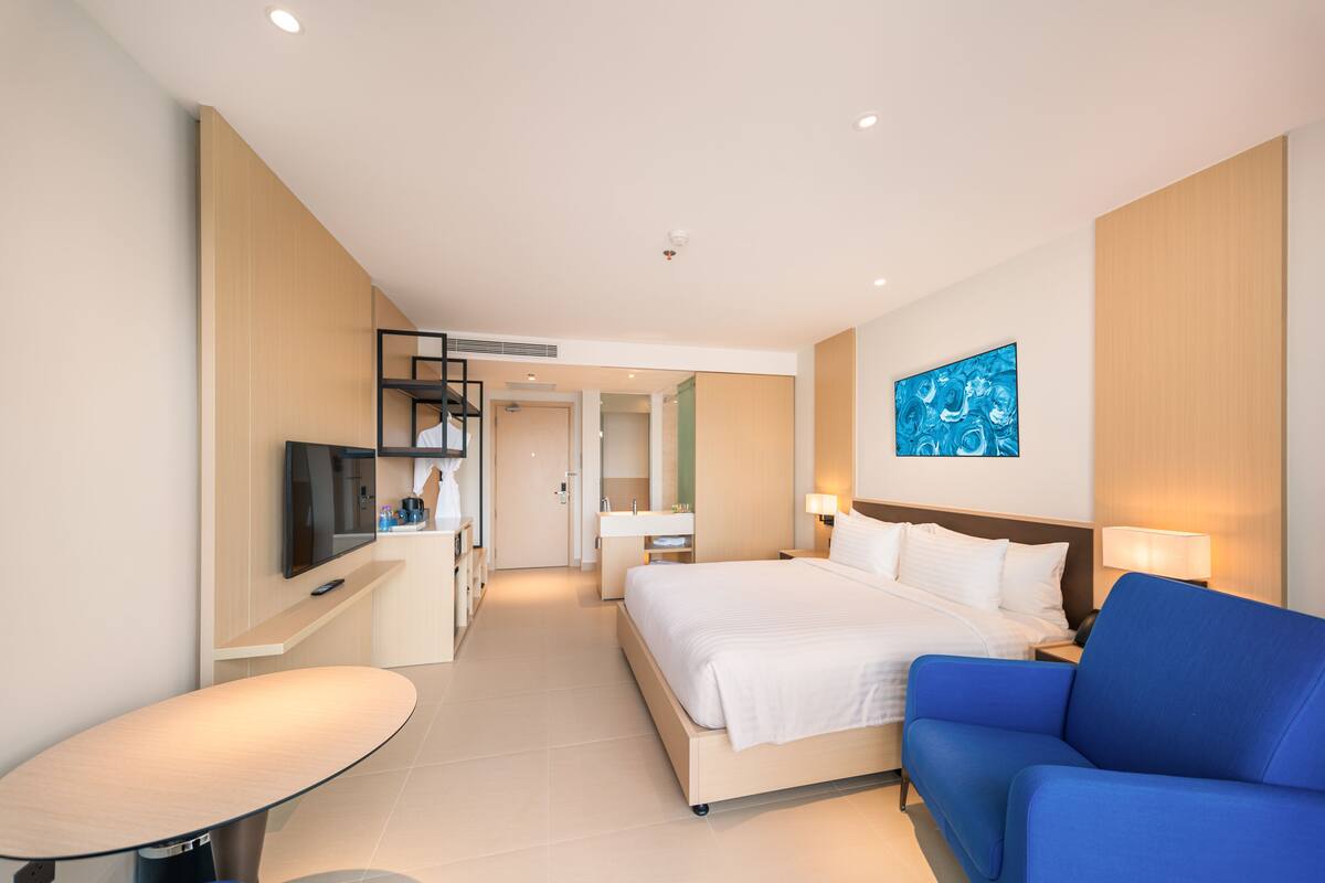 Una habitación de hotel moderna con una cama, un sillón azul, un televisor y un escritorio con una computadora.