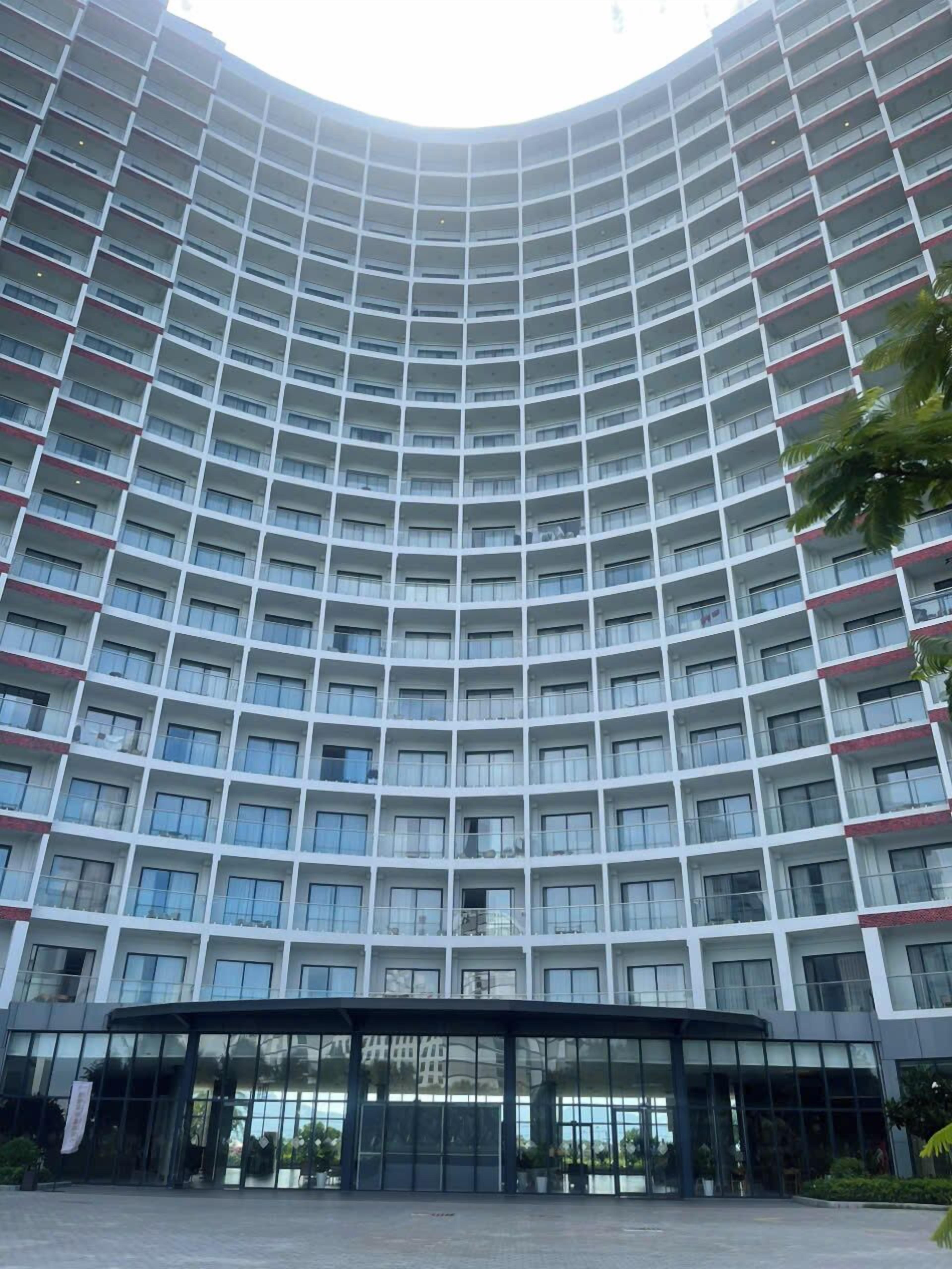 Un hotel de varios pisos con fachada curva, amplias ventanas de vidrio y un área de entrada cubierta.
