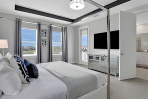 A modern hotel room with a large bed, a TV, a balcony with a view, and a bathroom with a mirror and sink.
