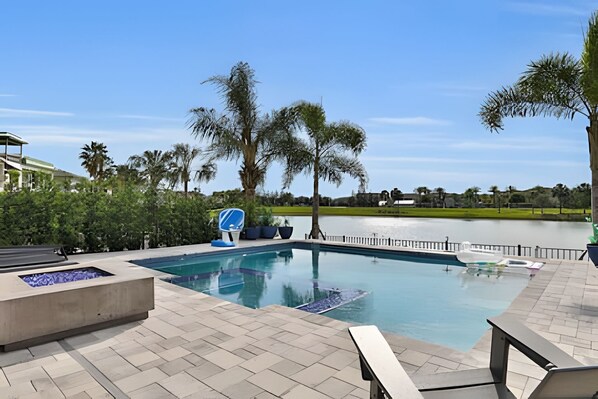 A swimming pool with a view of a lake, surrounded by palm trees and a paved deck.