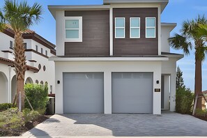 A modern two-story house with two garage doors, a flat roof, and a landscaped front yard with palm trees.