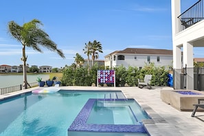 A swimming pool with a view of a lake, surrounded by palm trees and a building with a white facade.
