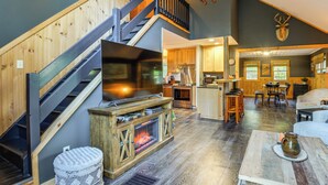 A spacious living area with a fireplace, wooden staircase, and a kitchen in the background. - Fishing Pond + Pool! Resort Retreat in Wilmington (Wilmington)