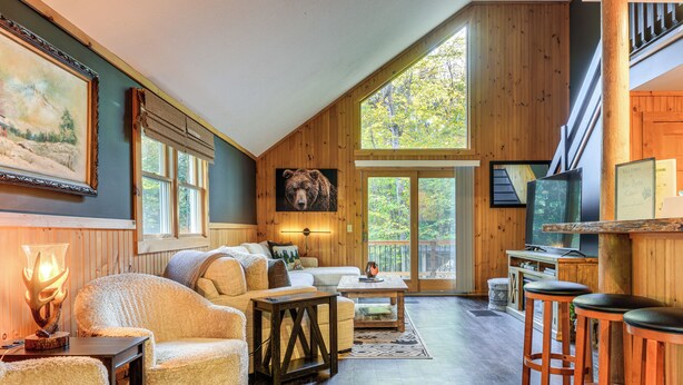 A cozy cabin interior with a large bear painting, a fireplace, and a wooden dining area. - Fishing Pond + Pool! Resort Retreat in Wilmington (Wilmington)