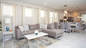 A modern living room with a sectional sofa, a coffee table, and a dining area with chairs and a table. - BR Villa w/ Pool, Star Wars Game Room + Resort (Davenport)