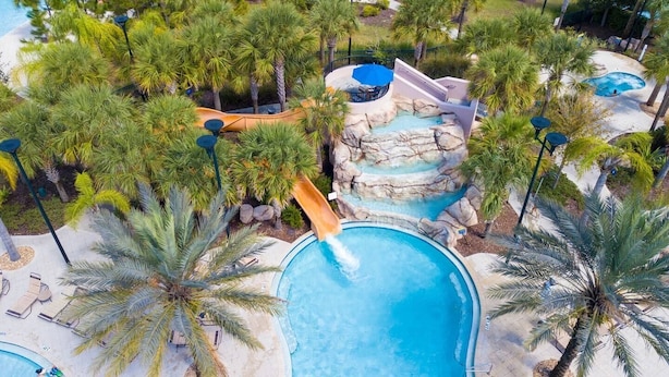 A resort pool area with a water slide, palm trees, and lounge chairs. - BR Villa w/ Pool, Star Wars Game Room + Resort (Davenport)